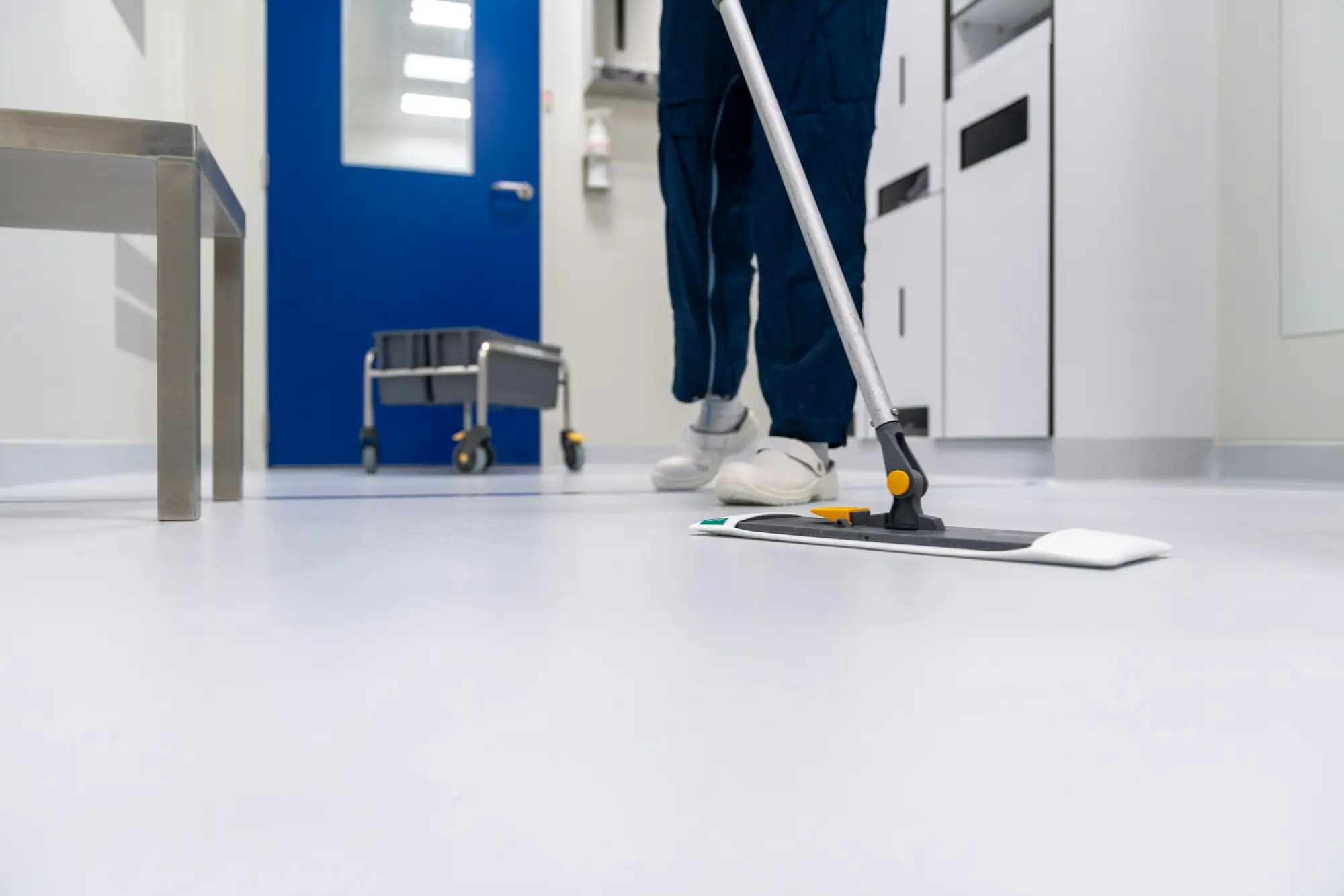 Cleaner mopping a bright white floor in a clinical hallway