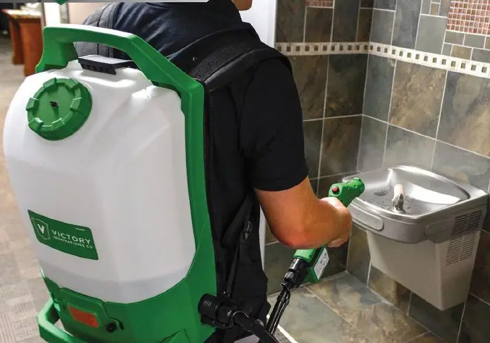 EnviroKleen technician disinfecting a restroom with a backpack electrostatic sprayer
