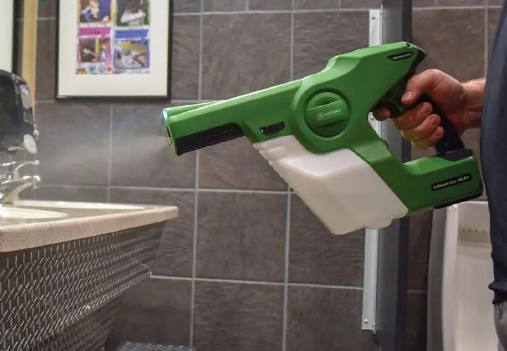 Handheld electrostatic sprayer misting a restroom counter