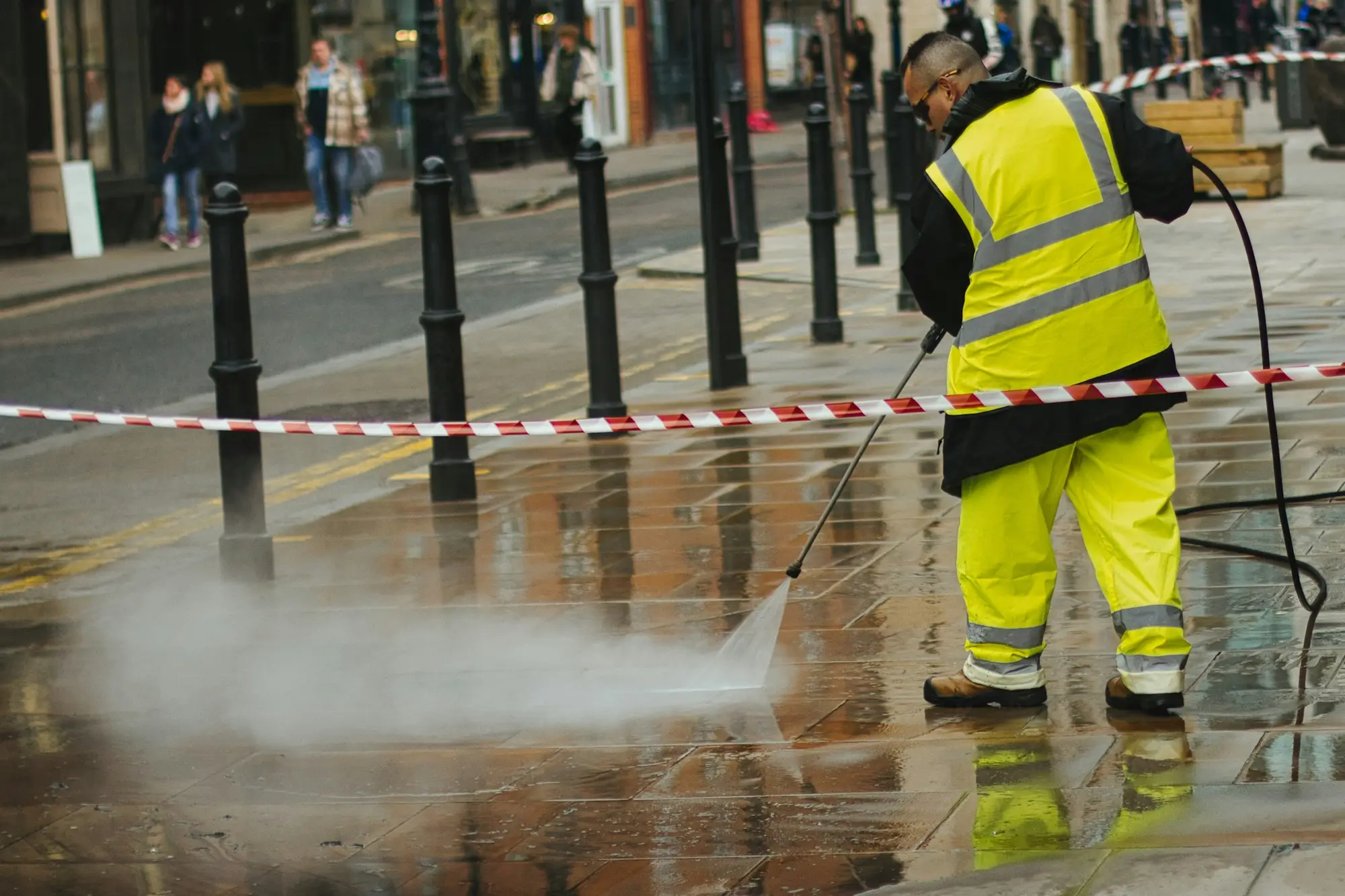 Worker in high-visibility gear pressure washing a paved walkway